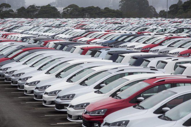 estacionamento ao ar livre de montadora com dezenas de automóveis zero quilômetro da mesma marca e modelo